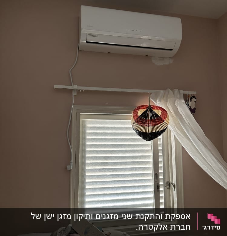 מזגן מותקן על קיר מעל חלון עם וילון לבן